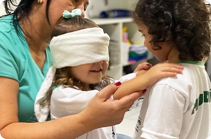 criança com venda nos olhos apoiando a mão no ombro de outra criança